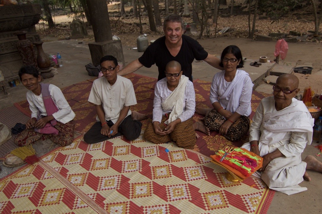 Steve Bender stands behind five temple elders and nuns seated on a woven mat, all wearing their new reading glasses