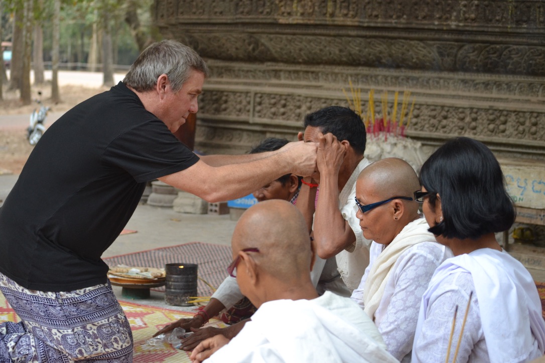 Steve Bender fits a pair of reading glasses on a man seated with nuns in white robes at a temple